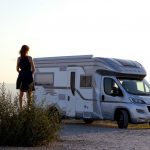 woman in black dress standing beside white and blue rv trailer during daytime