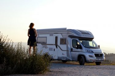 woman in black dress standing beside white and blue rv trailer during daytime