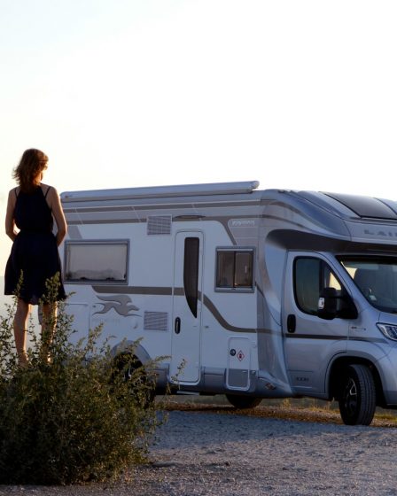 woman in black dress standing beside white and blue rv trailer during daytime
